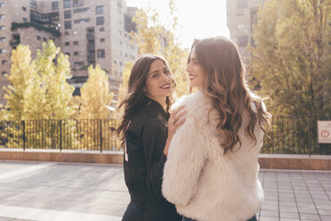 Twin sisters, walking outdoors, looking over shoulder, smiling - CUF04550