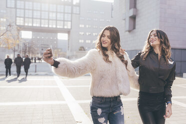 Twin sisters, walking outdoors, taking selfie, using smartphone - CUF04557