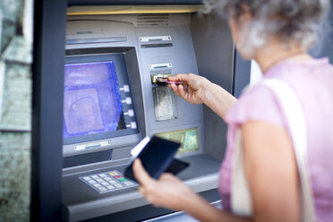 Reife Frau beim Einführen einer Kreditkarte in einen französischen Geldautomaten - CUF04601