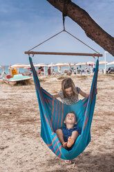 Mädchen schiebt ihren Bruder in der Hängematte am Strand von Poetto, Cagliari, Italien - CUF04698