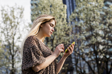 Junge Frau schaut in der Stadt auf ihr Smartphone - CUF04727