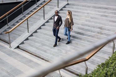 Young businessman and woman moving down city stairway talking - CUF04736