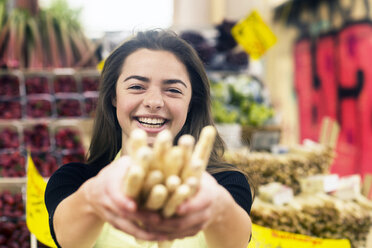 Portrait of young female stall trader holding bunch of breadsticks - CUF04744