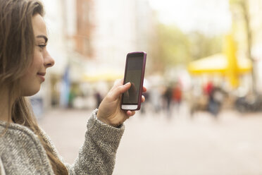 Junge Frau schaut in der Fußgängerzone auf ihr Smartphone - CUF04746