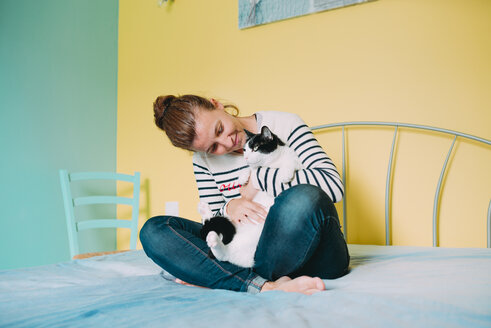 Glückliche Frau mit einer schwarz-weißen Katze auf dem Bett - GEMF01969