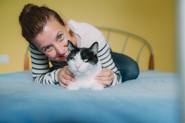 Glückliche Frau mit einer schwarz-weißen Katze auf dem Bett - GEMF01970