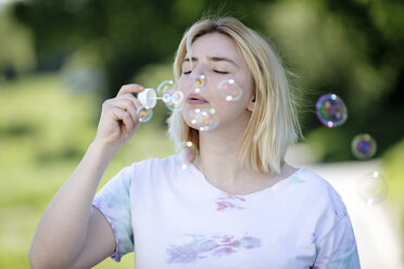 Young blonde woman blowing soap bubbles outdoors - FLLF00042