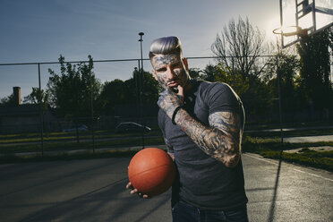 Portrait of tattooed young man with basketball on court - ZEDF01434