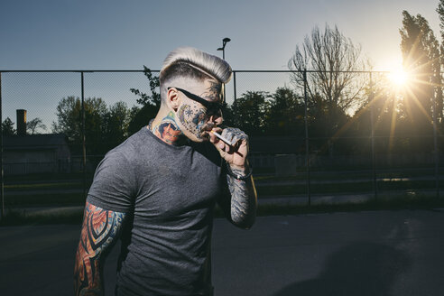 Tätowierter junger Mann mit Sonnenbrille, der eine Zigarette raucht - ZEDF01441