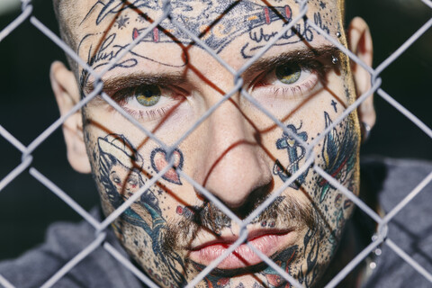 Tätowiertes Gesicht eines jungen Mannes hinter einem Zaun, lizenzfreies Stockfoto