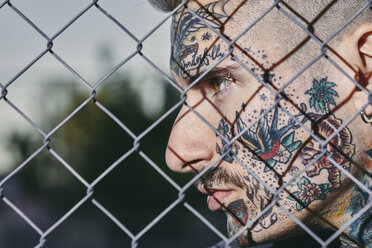 Tätowiertes Gesicht eines jungen Mannes hinter einem Zaun - ZEDF01457