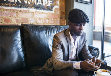 Businessman texting on sofa in cafe, London, UK - CUF04750