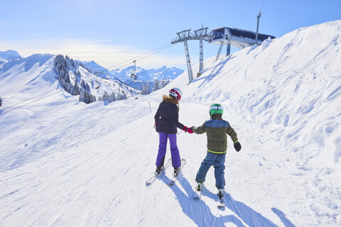 Rear view of girl and brother holding hands on ski slope, Gstaad, Switzerland stock photo