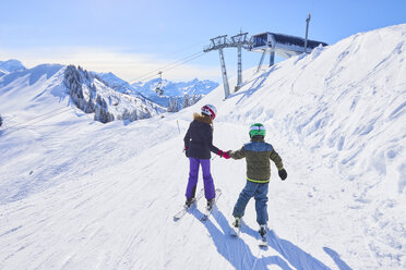 Rückansicht eines Mädchens und eines Bruders, die sich auf der Skipiste an den Händen halten, Gstaad, Schweiz - CUF04755