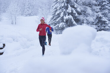 Female and male runners running on track in deep snow, Gstaad, Switzerland - CUF04768