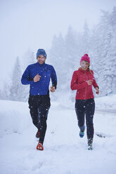 Female and male runners running in falling snow, Gstaad, Switzerland - CUF04774