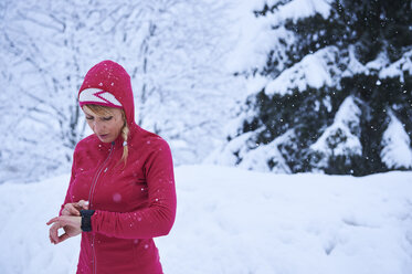 Läuferin mit rotem Kapuzenpulli und Smartwatch im Schnee, Gstaad, Schweiz - CUF04793