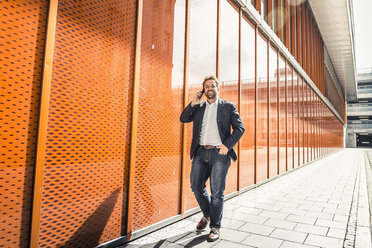 Businessman making smartphone call while strolling outside office building - CUF04800