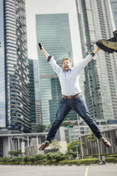 Happy businessman jumping for joy by city skyscrapers - CUF04808