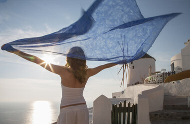 Frau mit erhobenen Armen, die einen Kaftan hält und über das Meer blickt, Santorin, Kykladen, Griechenland - CUF04812