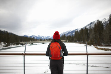 Hiker on bridge looking at snow capped mountains, Banff, Canada - CUF04818
