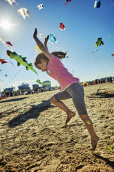 Young girl doing cartwheel on beach, kites flying in sky behind her, Rimini, italy - CUF04862