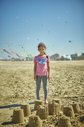 Porträt eines jungen Mädchens, das hinter Sandburgen am Strand steht, Rimini, Italien - CUF04863
