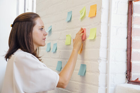 Woman sticking sticky notes to brick wall - ISF01182