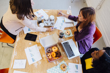 Colleagues working together at desk sharing doughnuts - ISF01217