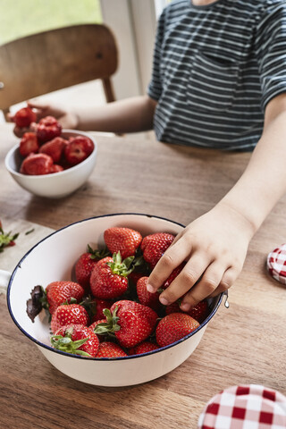 Junge nimmt Erdbeere aus Schale, Mittelteil, Nahaufnahme, lizenzfreies Stockfoto