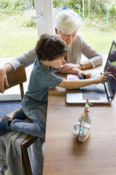 Großmutter und Enkel sitzen am Tisch und benutzen einen Laptop - ISF01283