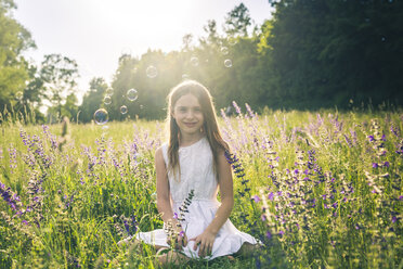 Portrait of smiling girl crouching on flower meadow at evening twilight - SARF03742
