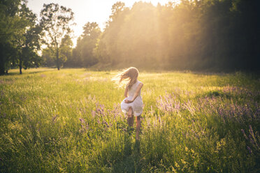 Rückenansicht eines Mädchens, das in der Abenddämmerung auf einer Blumenwiese läuft - SARF03744