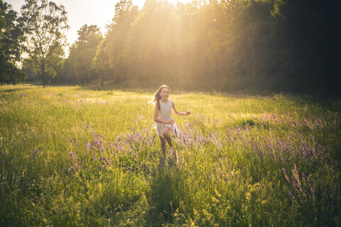 Smiling girl running on flower meadow at evening twilight stock photo