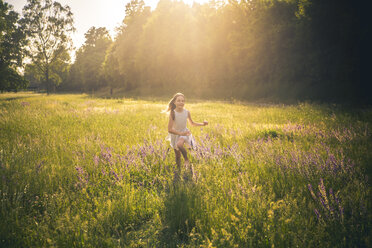 Smiling girl running on flower meadow at evening twilight - SARF03745