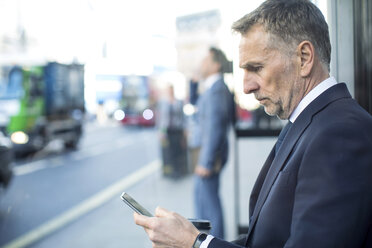 Businessman waiting at bus stop using smartphone, London, UK - CUF04895