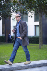 Mann mit Smartphone und Kopfhörern beim Spaziergang im Freien - CUF04907