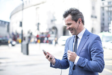 Businessmen in street with smartphone and earbuds, London, UK - CUF04916