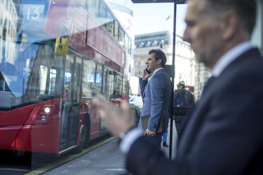 Geschäftsmann wartet an der Bushaltestelle und benutzt sein Smartphone, London, UK - CUF04919