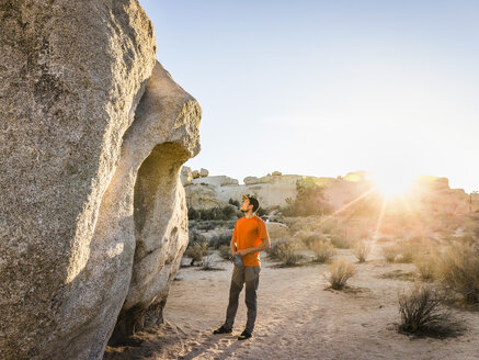 Männlicher Boulderer schaut in der Abenddämmerung zu einem Felsbrocken im Joshua Tree National Park, Kalifornien, USA - CUF04926