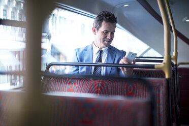 Geschäftsmann schaut im Doppeldeckerbus auf sein Smartphone - CUF04938