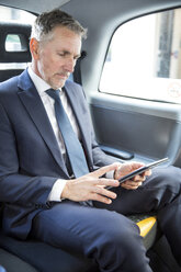 Mature businessman looking at digital tablet in taxi cab - CUF04944