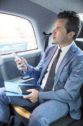 Mature businessman holding smartphone in taxi cab - CUF04945