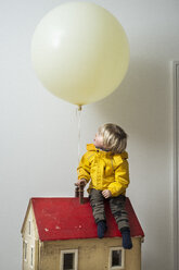 Junge sitzt auf einem Puppenhaus und schaut auf einen Luftballon - CUF04951