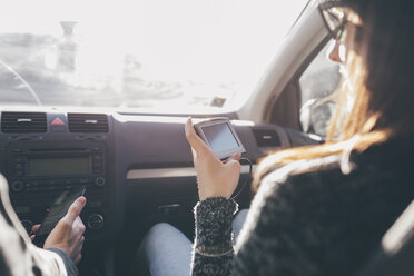 Blick über die Schulter auf eine Frau, die auf dem Vordersitz eines Autos auf ein Navigationsgerät schaut - CUF04952