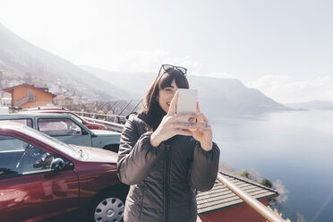 Mittlere erwachsene Frau macht Smartphone-Selfie am Seeufer, Monte San Primo, Italien - CUF04953