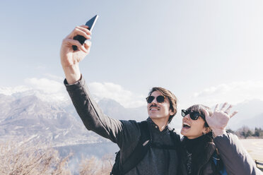 Couple taking smartphone selfie above mountain lakeside, Monte San Primo, Italy - CUF04962