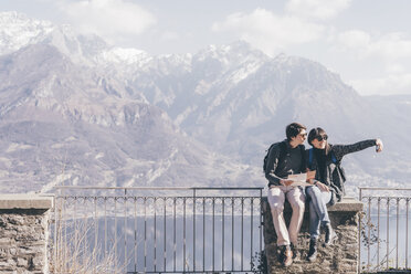 Paar sitzt auf einer Terrassenmauer mit Blick auf einen Bergsee, Monte San Primo, Italien - CUF04965
