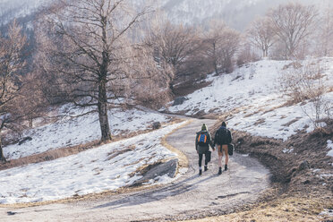 Rückansicht eines wandernden Paares auf einer verschneiten Landstraße, Monte San Primo, Italien - CUF04980