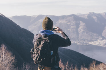 Rear view of male hiker photographing lake and mountains, Monte San Primo, Italy - CUF04981